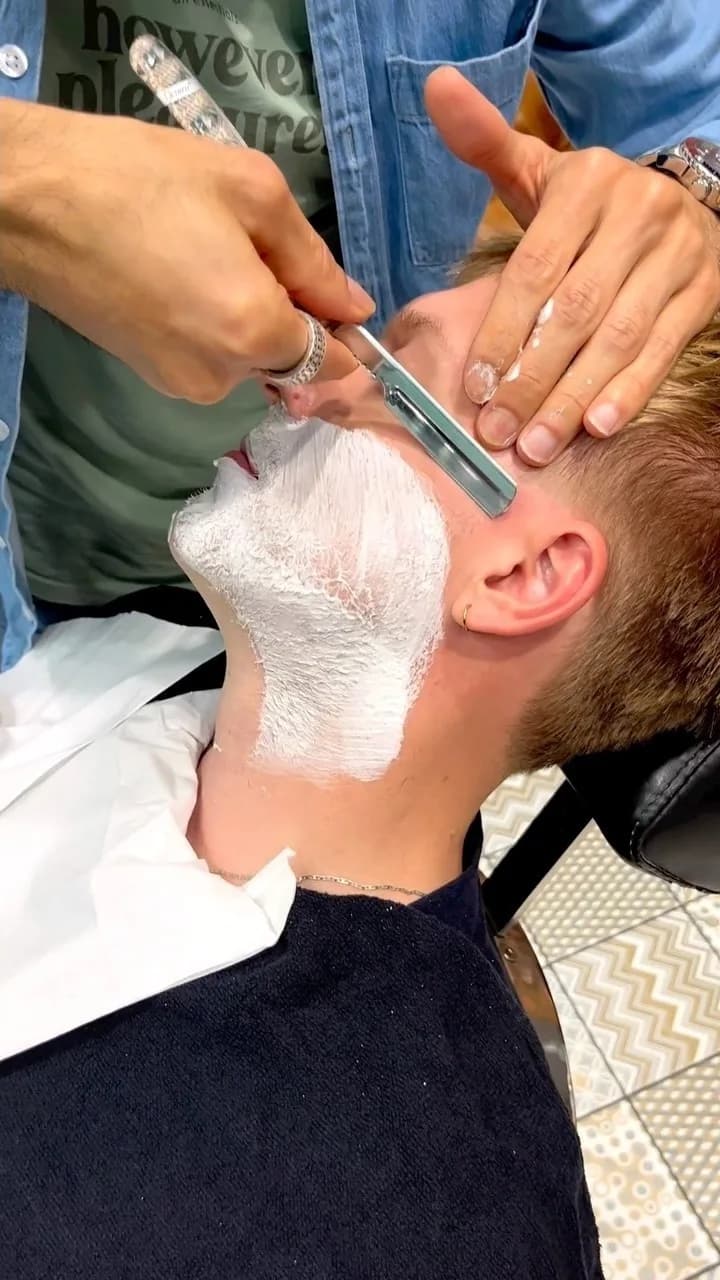 Rasage traditionnel au coupe-chou sur la joue couverte de mousse d’un client